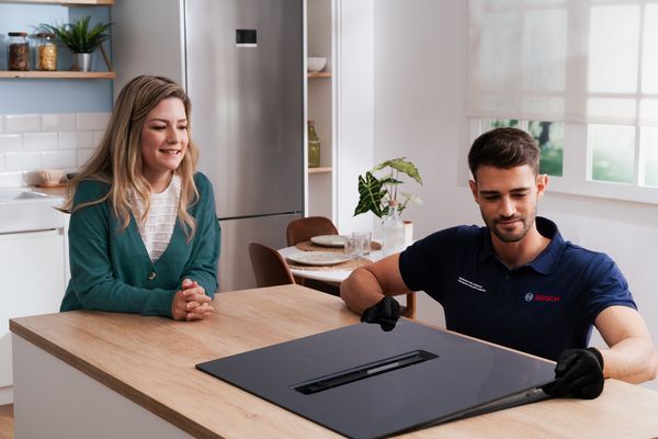 En Bosch-servicetekniker visar en induktionshäll med integrerad fläkt för en nöjd kund i hennes kök.