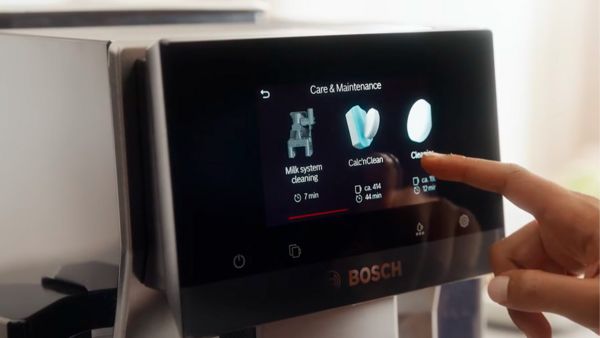 Écran tactile d'une machine Bosch montrant des options pour l'entretien. Un utilisateur touche l'option "CalcioClean" pour le nettoyage du système de lait.