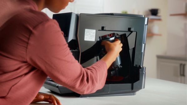L'image montre une personne manipulant le réservoir ou le groupe de percolation à l'arrière d'une machine à café Bosch. Cela fait partie du processus d'entretien ou de nettoyage de l'appareil, essentiel pour assurer son bon fonctionnement.