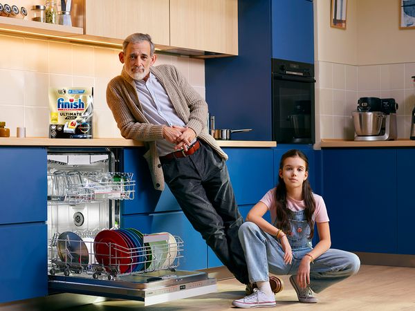 Adult and child in kitchen next to open Dishwasher with Finish bundle on top