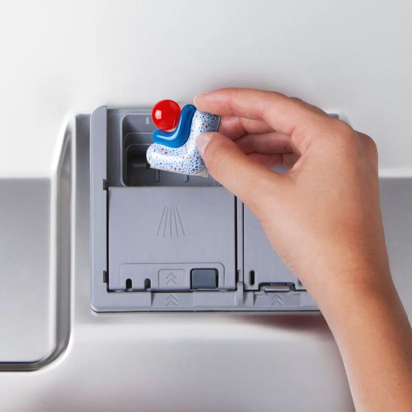 Hand placing a dishwasher tablet in the detergent compartment inside the dishwasher door.