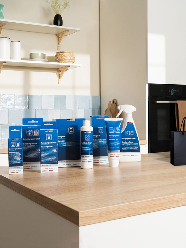 Uma bancada de cozinha brilhante que exibe uma variedade de produtos de limpeza Bosch em embalagens azuis, juntamente com itens decorativos e um vaso escuro.