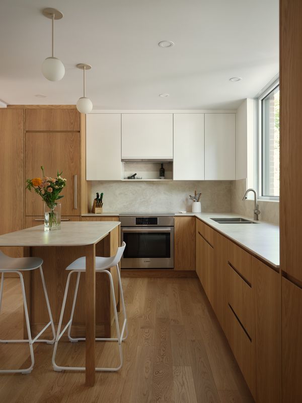Une cuisine moderne avec des armoires en bois, des plans de travail blancs, et une table à manger avec deux tabourets, illuminée par des suspensions.