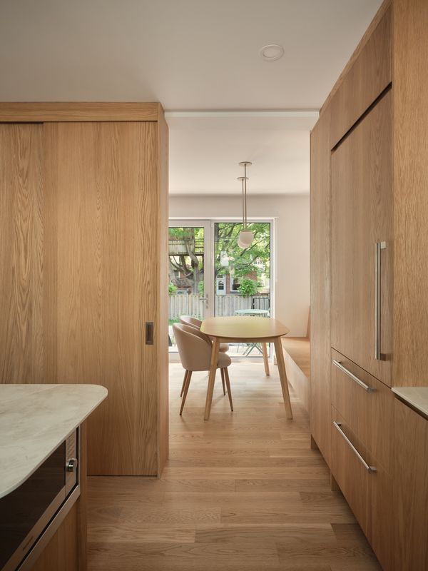 Une cuisine moderne avec des armoires en bois, une petite table à manger et de grandes fenêtres donnant sur un jardin luxuriant. La lumière naturelle inonde l'espace.