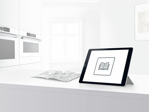 Planšetdators uz virtuves galda ar grāmatas ikonu, kas simbolizē Bosch lietotāja rokasgrāmatu