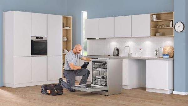 Boîte à outils et tablette représentant la hotline Réparation sur une table de cuisine avec un réfrigérateur Bosch en arrière-plan 