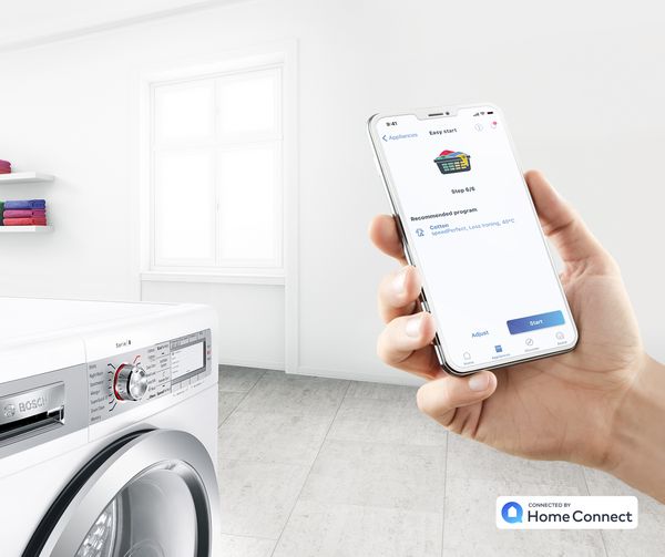 Smartphone avec l'application Home Connect ouverte devant un lave-linge Bosch. 