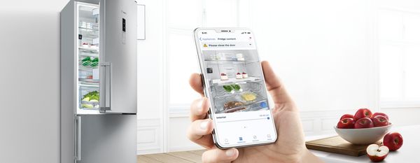 Hand Holding Smartphone with Home Connect app on screen in open plan room with Bosch Products