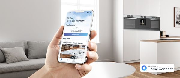 Smartfon z aplikacją Home Connect oraz piekarniki marki Bosch w tle. 