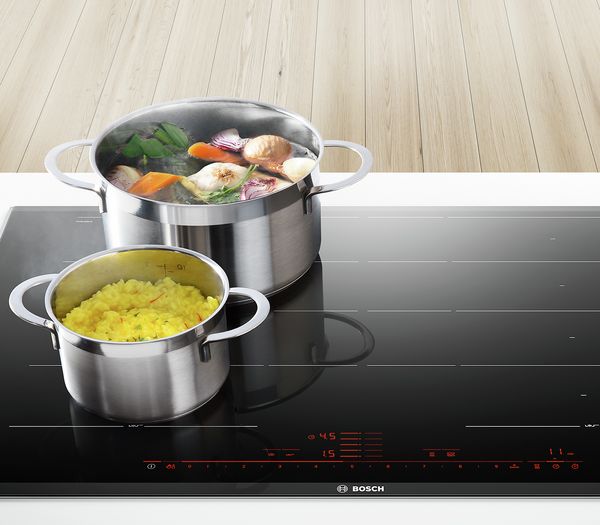 A roasting pan of vegetables sits on an induction cooktop.