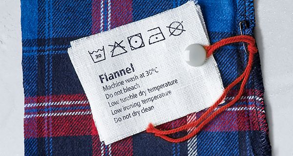 Neun aus Kleidungsstücken ausgeschnittene Etiketten mit Waschsymbolen.