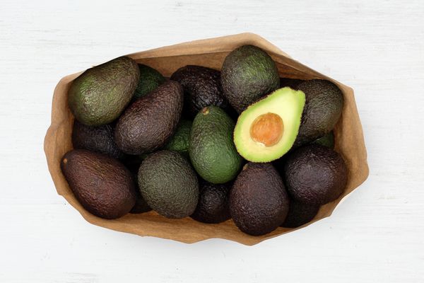 Bunke af diverse avocadoer med halverede avocadoer øverst i en brun indkøbspose.