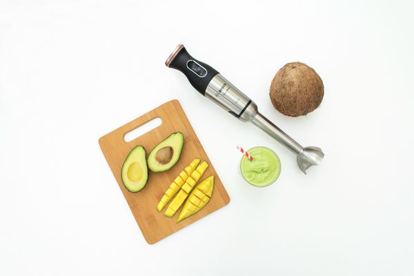 En lækker avocadosmoothie med en halveret avocado, mango og kokosnød ved siden af en sølvfarvet blender fra Bosch.