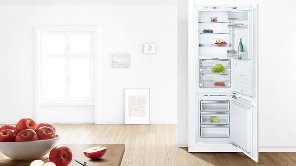 Bosch 60/40 -jääkaappipakastin valkoisessa keittiössä ovet auki ja ruokaa sisällä. Etualalla kulhollinen omenoita.