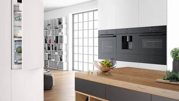 Cucina moderna in bianco, con elettrodomestici Bosch e piano in legno con grappoli d'uva. Frigorifero con porta socchiusa. 