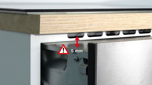 5 mm:n etäisyys näkyy uunin yläosan, työtason ja keittotason alaosan lähikuvassa. Punainen kaksipäinen nuoli ja punainen varoitusmerkki.