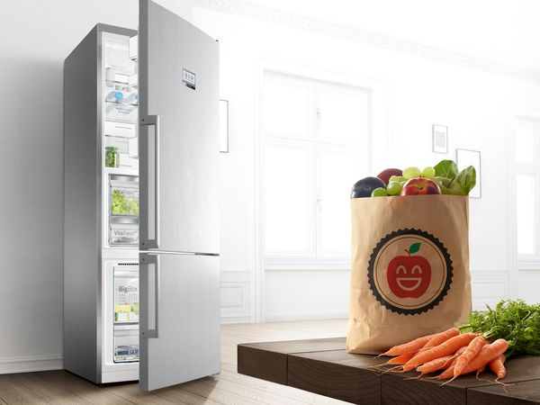 Slightly open fridge freezer door with bag of vegetables nearby