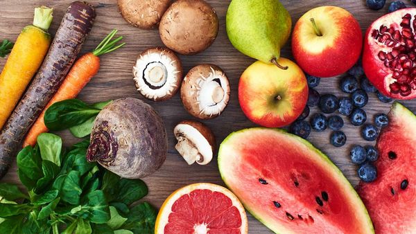 Auf einer Küchenarbeitsplatte aus Holz befinden sich aufgeschnittenes Obst, Äpfel, Birnen, Beeren, Pilze, Rüben in verschiedenen Farben, Rote Beete sowie Feldsalat.