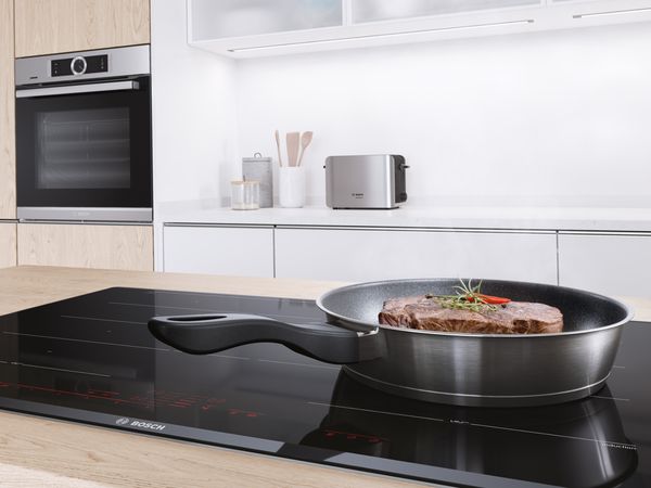 現代開放式廚房，配有三件齊胸高的嵌入式電器和在島式煮食爐上滋滋作響的平底鍋