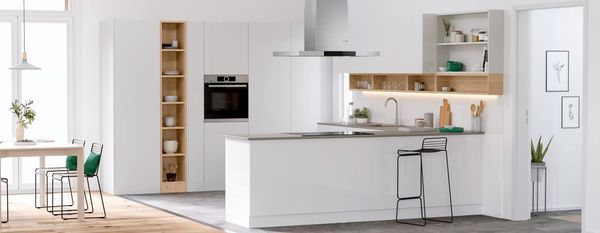 Musta Bosch-uuni, liesituuletin ja keittotaso sekä kalusteisiin sijoitettava astianpesukone ja jääkaappi modernin valkoisessa IKEA-keittiössä.