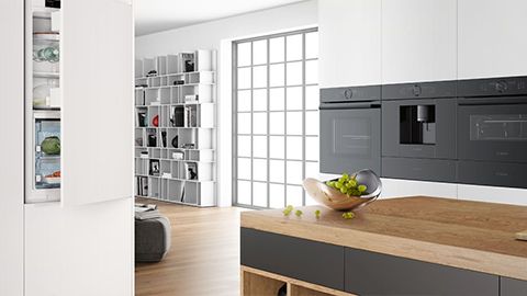 Modern fehér konyha, fekete Bosch készülékekkel, és matt fekete fiókos tölgyfa központi konyhaszigettel
