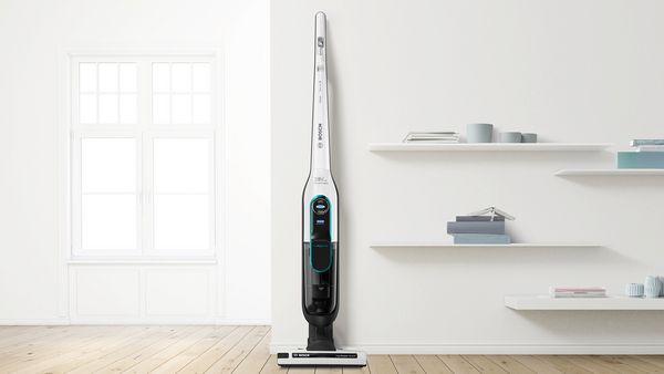 A Bosch Athlet vacuum is standing in a living room. There's a couch behind it.