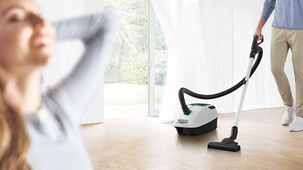 Compact grey cylinder vacuum on a white rug with floor-length windows in the background 