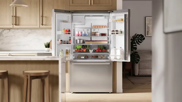 Frigo ouvert, rempli d'aliments, de boissons et de fruits et légumes frais, dans une cuisine moderne avec des armoires en bois.