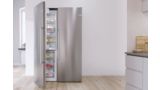 Silver freestanding side-by-side Bosch fridge in a white kitchen. Open door shows fresh food.