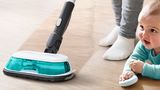 Mopping vacuum cleans the floor while a baby plays nearby.