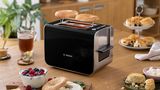 Reheat two slices of bread on the Styline toaster, set on a kitchen counter surrounded by hot drinks and dishes.