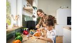 A young man slides a drawer filled with raw food into his Bosch Air Fryer, preparing for cooking in a bright kitchen.