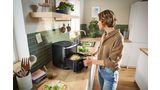 A young man places a plate of freshly cooked food on the kitchen counter. A second plate and a bowl of cucumber salad sit next to it.