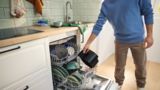 Um homem carrega a gaveta vazia da sua Air Fryer da Bosch para a máquina de lavar loiça na sua cozinha moderna.