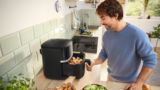 Um jovem coloca uma gaveta cheia de alimentos crus na sua Air Fryer da Bosch, preparando-se para cozinhar numa cozinha luminosa.