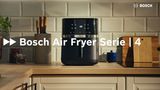 A Air Fryer da Bosch fica numa bancada de cozinha com a gaveta aberta, revelando um monte de asas de frango douradas no interior, rodeadas por pratos de vários alimentos deliciosos, como legumes assados estaladiços e suculentos filetes de salmão.