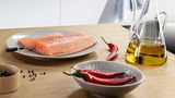 Brezžična sonda za meso, vstavljena v velik file lososa, ki leži na krožniku in je obdan s kuharskimi sestavinami.