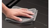Hand met grijze doek maakt strak zwart oppervlak van inductiekookplaat schoon.