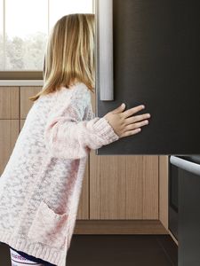 Klein kind dat in een grote koelkast kijkt, met haar hand op de zwarte roestvrijstalen deur.