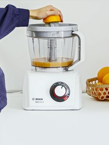 Person squeezing half an orange on top of food processor to release juice
