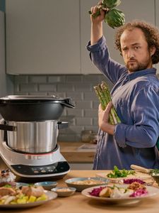 Un homme danse à côté de son Cookit, des légumes verts dans chaque main, tout en cuisinant sa propre recette.  