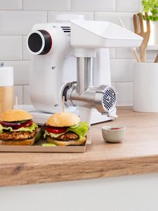 Zwei selbstgemachte Burger befinden sich appetitlich angerichtet vor einer Bosch Küchenmaschine mit Fleischwolfaufsatz.