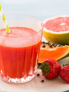 A fresh juice with red fruits in the background.