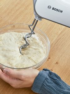 A person kneading a dough with the Bosch hand mixer.