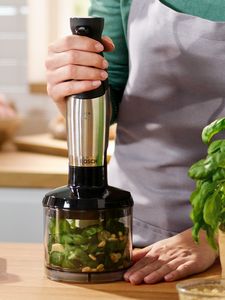 A person holds a Bosch hand blender, using the chopper accessory to cut up vegetables.