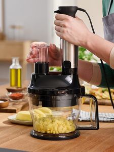 A hand operates a blender fitted to the cube cutter accessory, which rests on a wooden counter and is dicing potatoes.