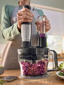 A person in an apron uses a food processor to shred red cabbage.