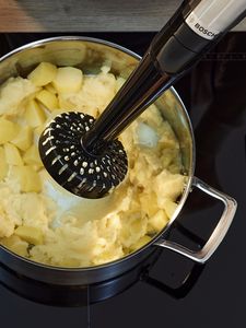Un blender avec le presse-purée plane au-dessus d'une casserole de cubes de pommes de terre fraîchement cuits.