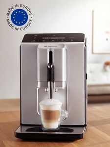 VeroCafe Gerät auf der Küchenarbeitsplatte mit einer Tasse Cappuccino und der Europa-Flagge in der oberen Bildecke.