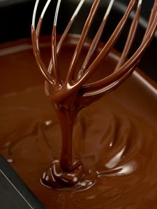 A pan of melted chocolate with a whisk from which the melted chocolate drips.